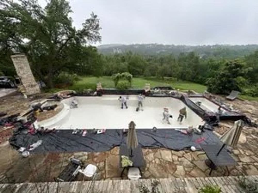 Construction crew applying waterproof sealant to an empty swimming pool in a residential backyard.