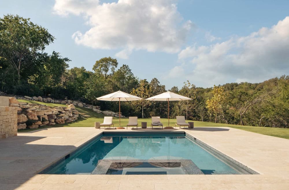 Modern backyard oasis with a sparkling pool, lounge chairs, and shaded umbrellas.