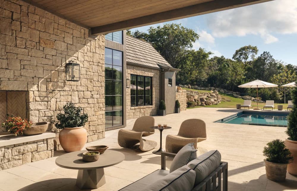 Elegant patio with stone wall, modern furniture, and a poolside oasis in a serene landscape.