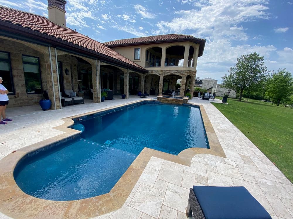 Luxury backyard with a swimming pool, stone patio, and a modern home under a blue sky.
