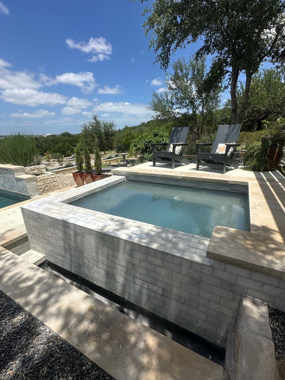 Modern outdoor hot tub with stone surround and lounge chairs overlooking scenic landscape.