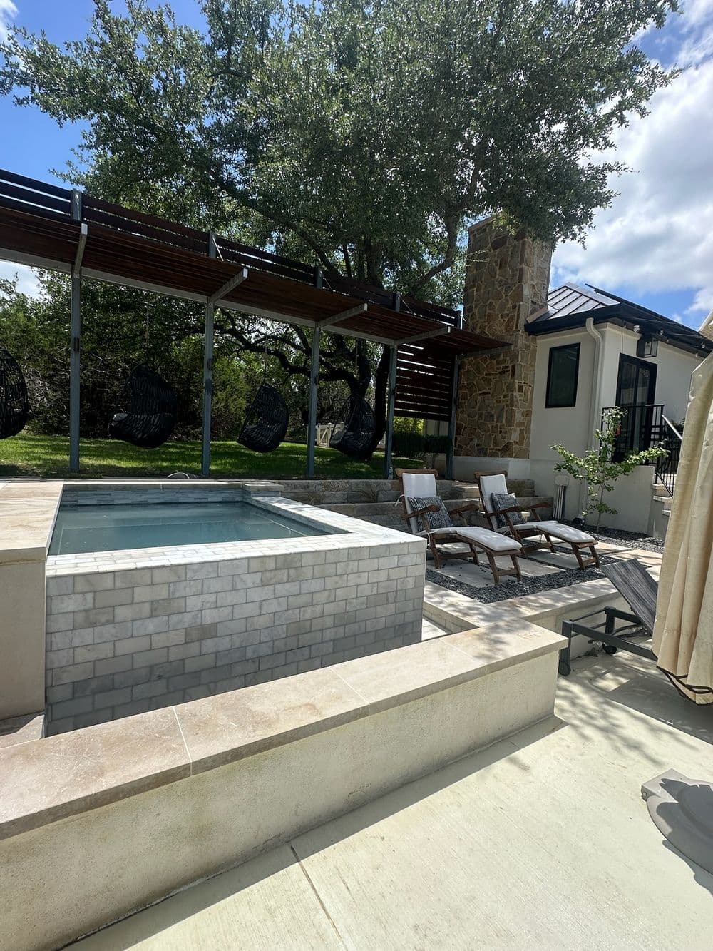 Modern patio with spa, lounge chairs, and shaded seating area among lush greenery.