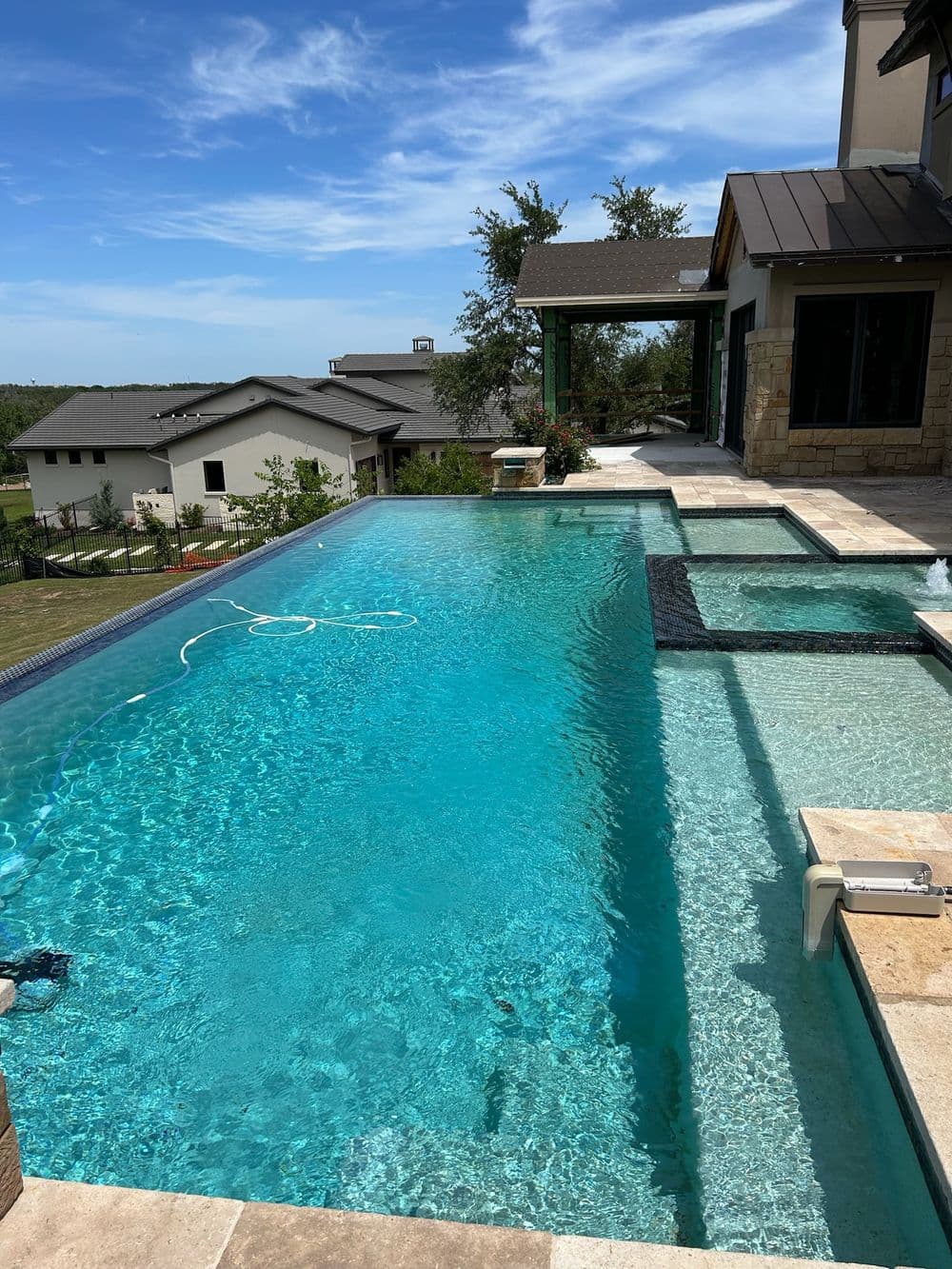 Luxury infinity pool with clear blue water overlooking scenic landscape and modern home.