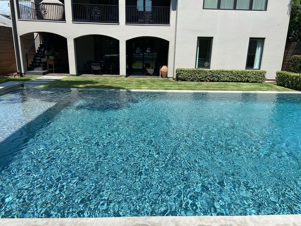 Luxury backyard pool reflecting sunlight with a modern home in the background. Perfect for relaxation.
