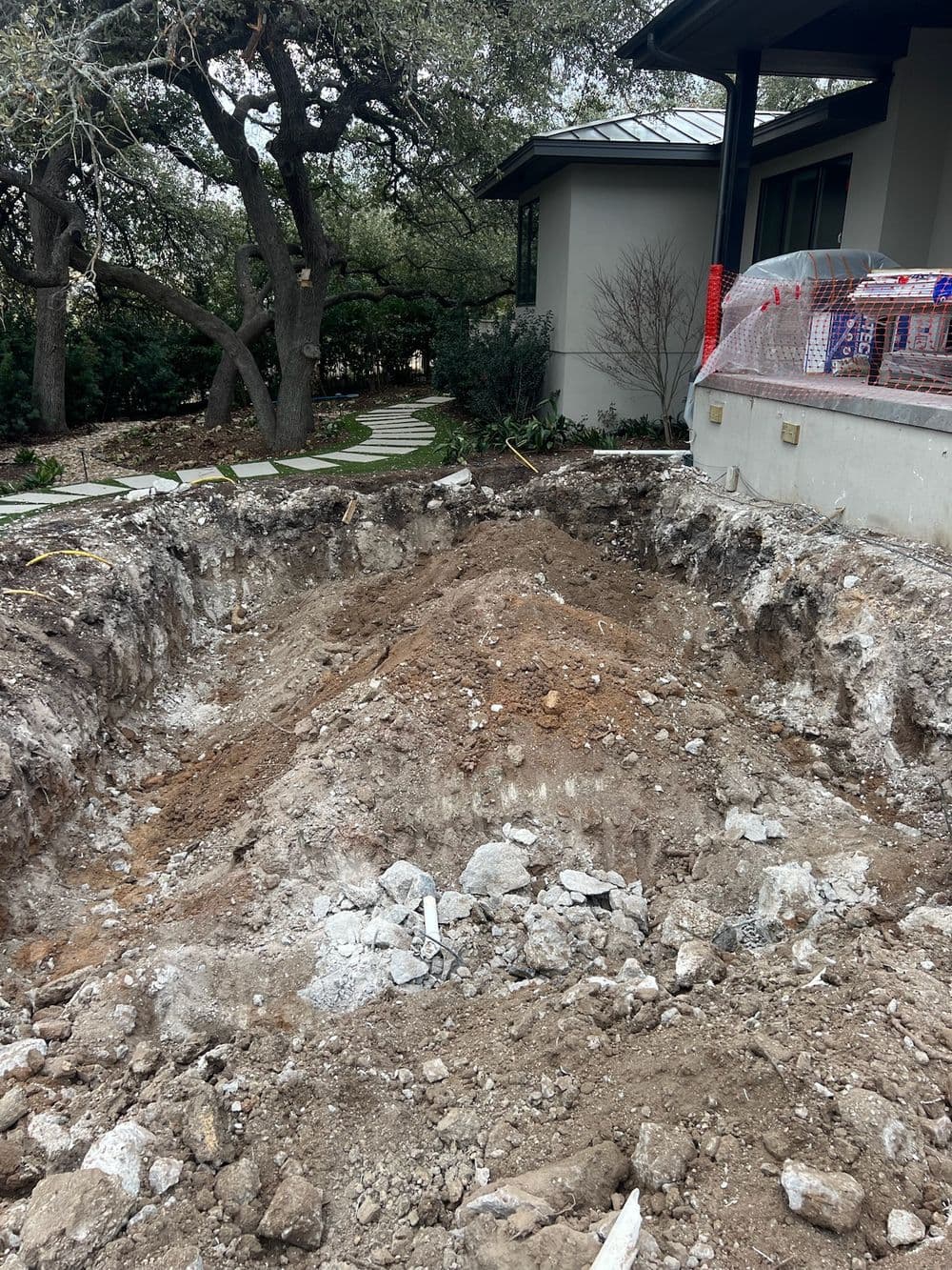 Excavated area showing dirt and rocks for construction near a modern home landscape.