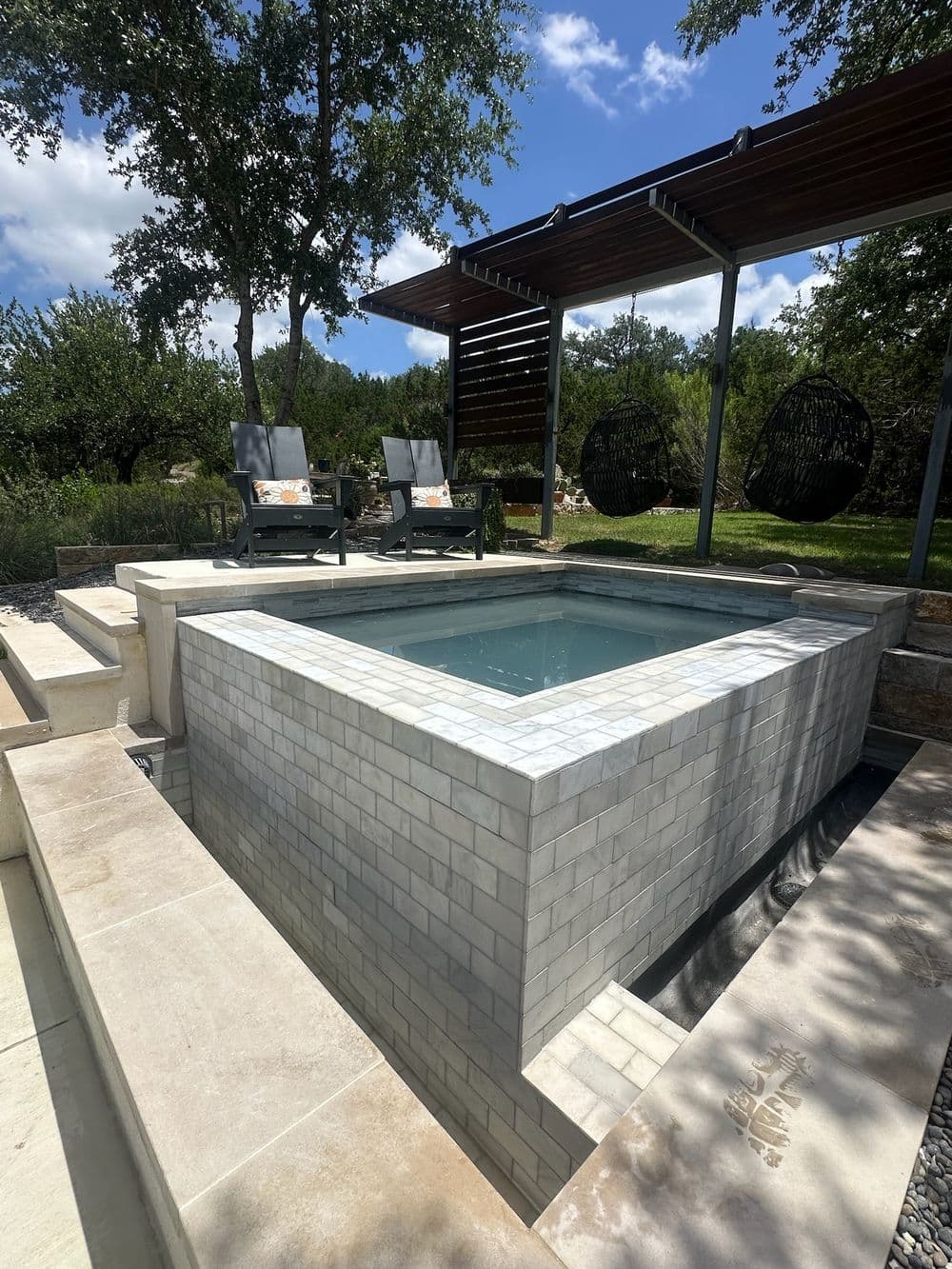 Modern outdoor spa in a serene garden setting with lounge chairs and shade structure.