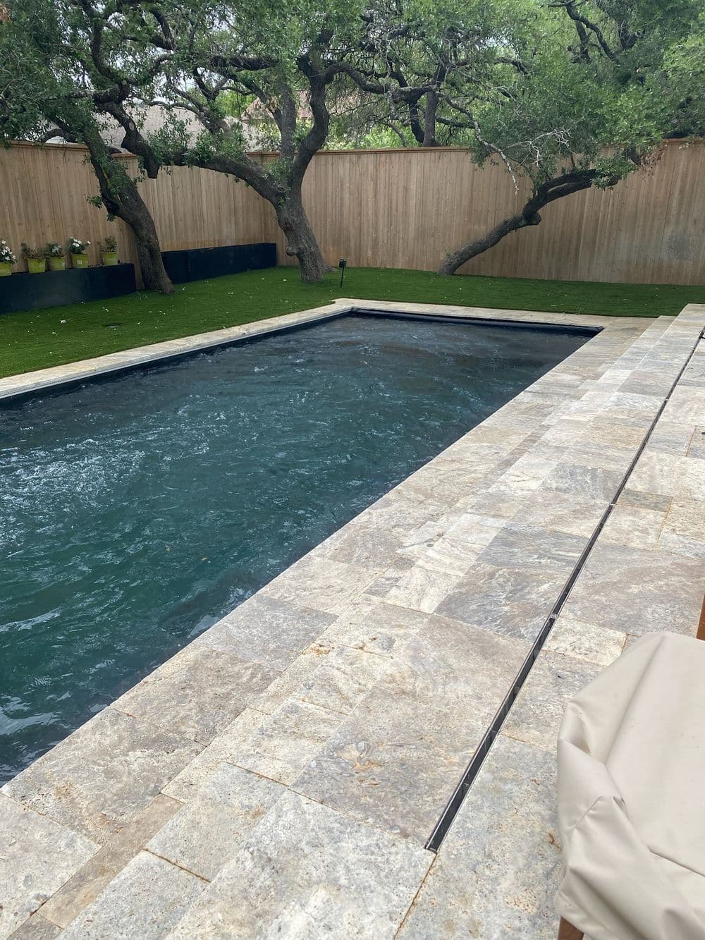 Modern outdoor swimming pool with natural stone surround, lush greenery, and wooden fence.