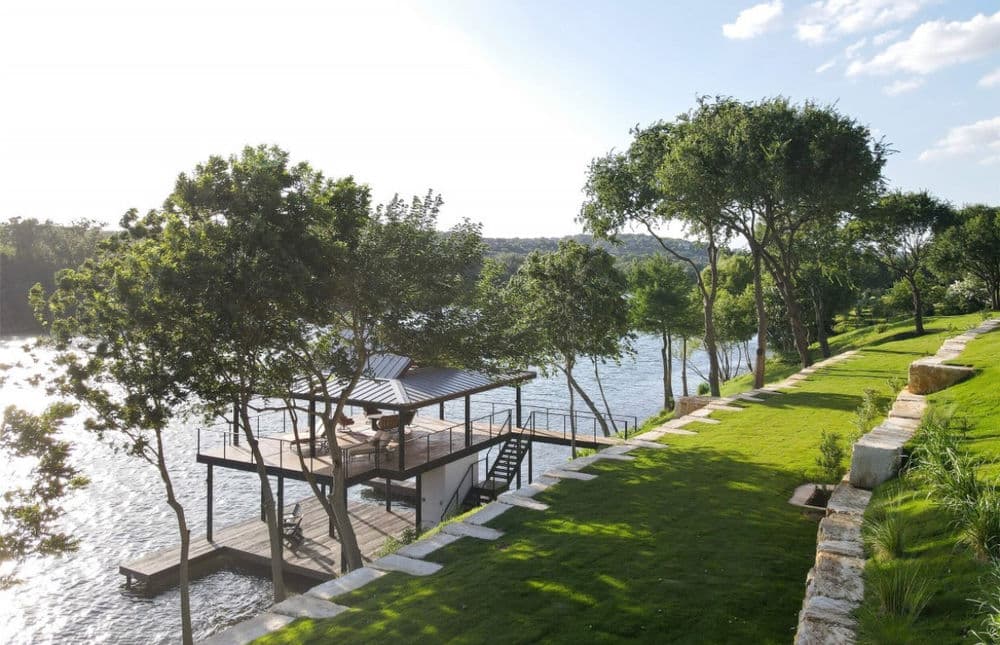 Scenic lakeside view with a wooden dock and lush greenery under a blue sky.
