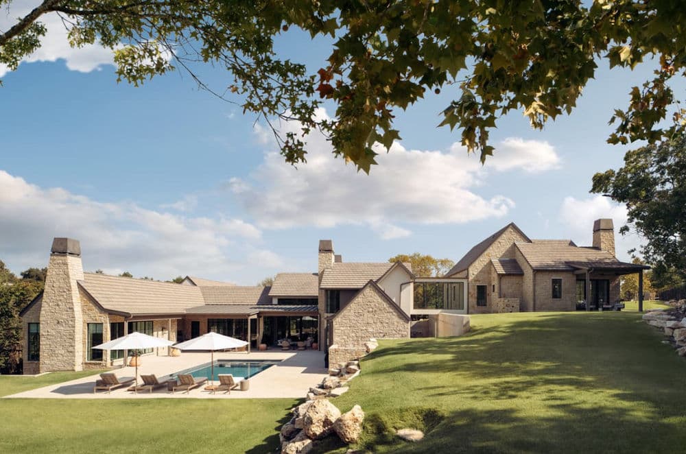 Modern stone house with landscaped lawn, pool area, and blue sky backdrop.