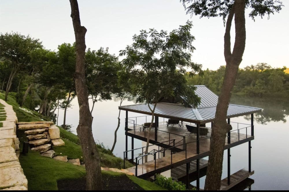 Scenic riverside pavilion with trees reflecting in calm water at sunrise.