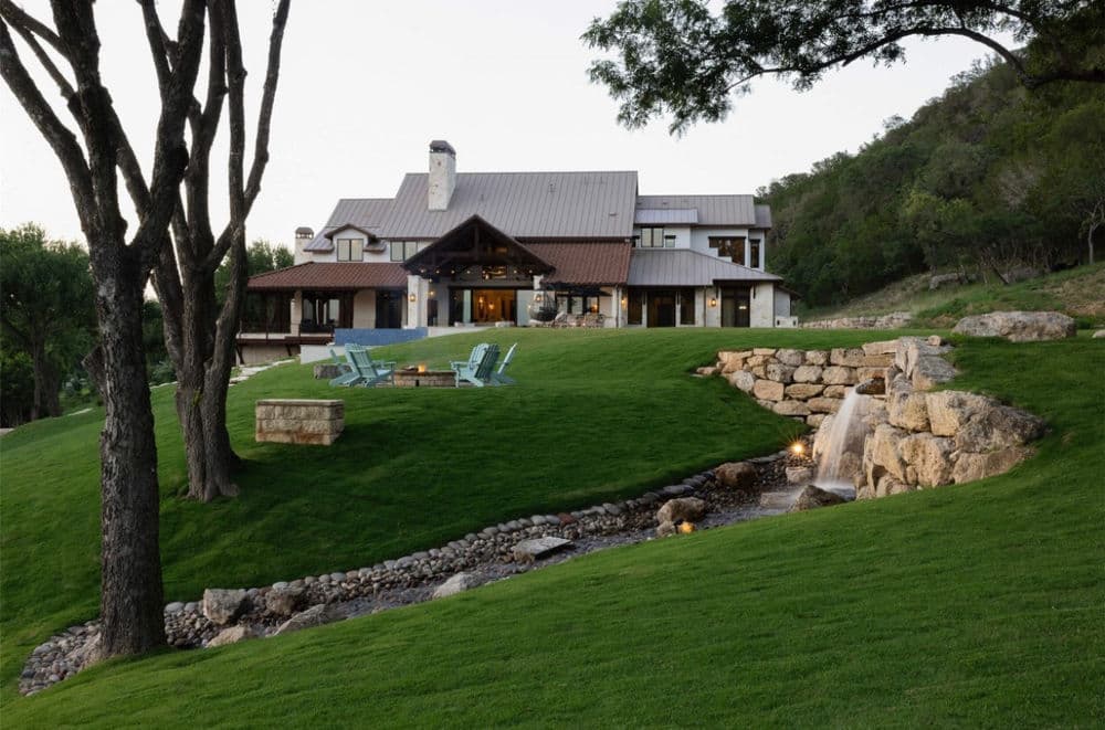 Luxurious home with a landscaped yard, stone waterfall, and outdoor seating area.