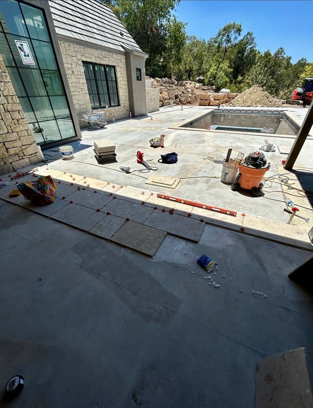 Construction site with laid tiles, pool under construction, and tools scattered around.