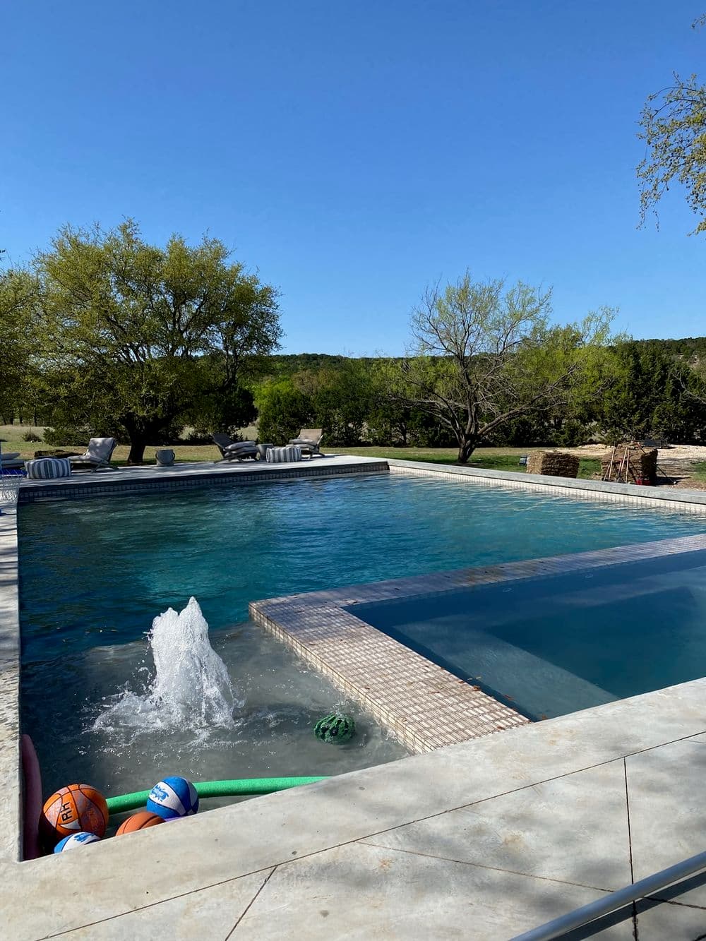 Scenic backyard pool with water features, vibrant trees, and colorful pool toys.