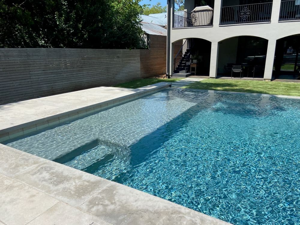 Modern backyard swimming pool with clear water and surrounding landscaped area.
