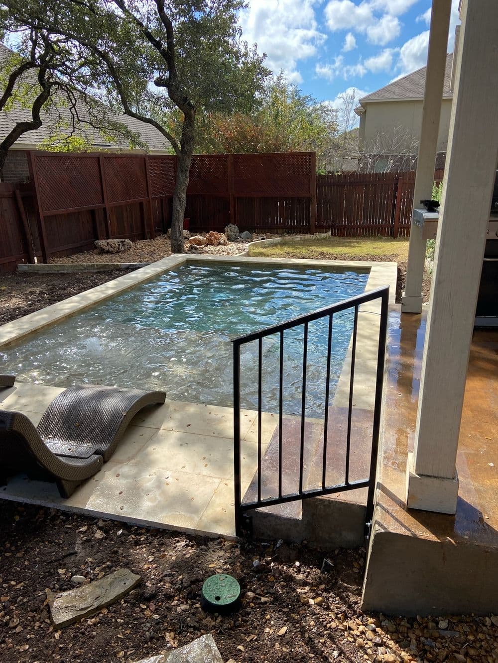 Backyard pool with lounge chair, surrounded by trees and wooden fence on a sunny day.