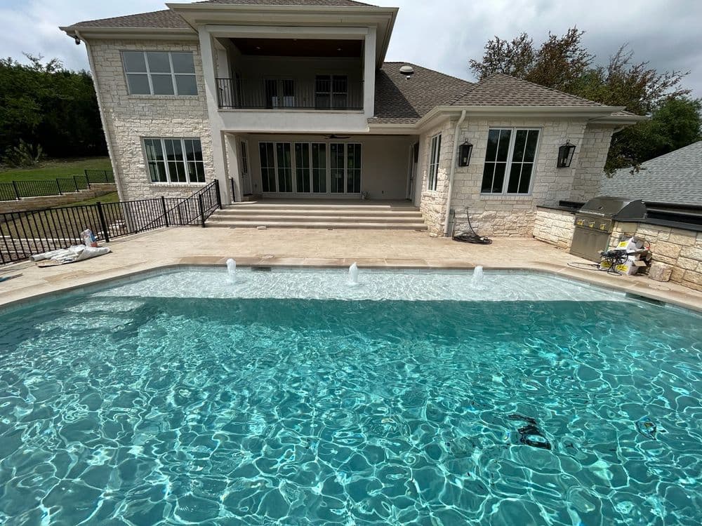 Luxury backyard pool with fountains, modern home facade, and stone patio. Ideal for relaxation.