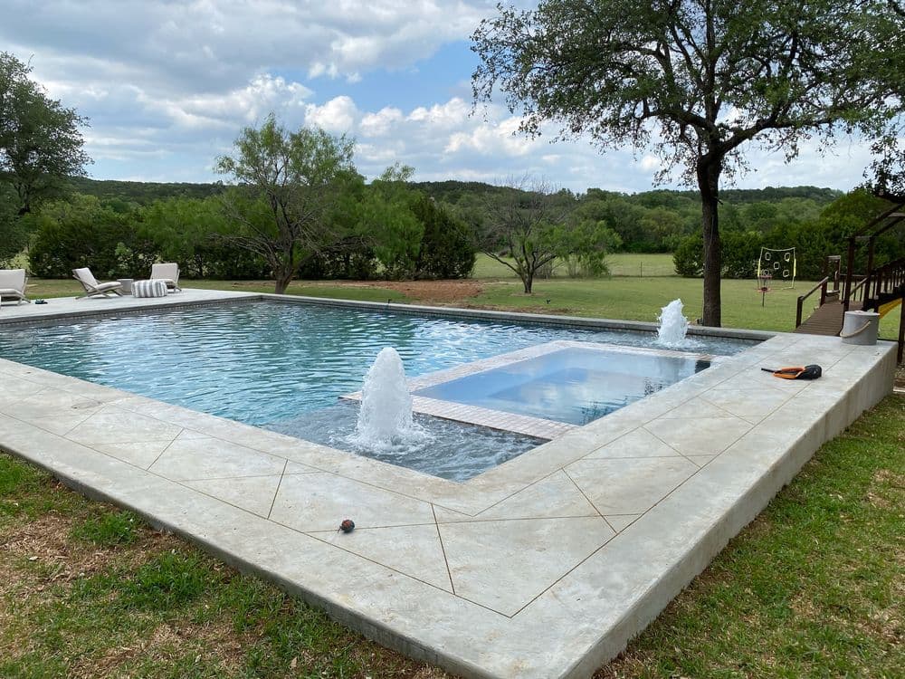 Luxury outdoor pool with water features and scenic backyard view. Relaxing spa area nearby.