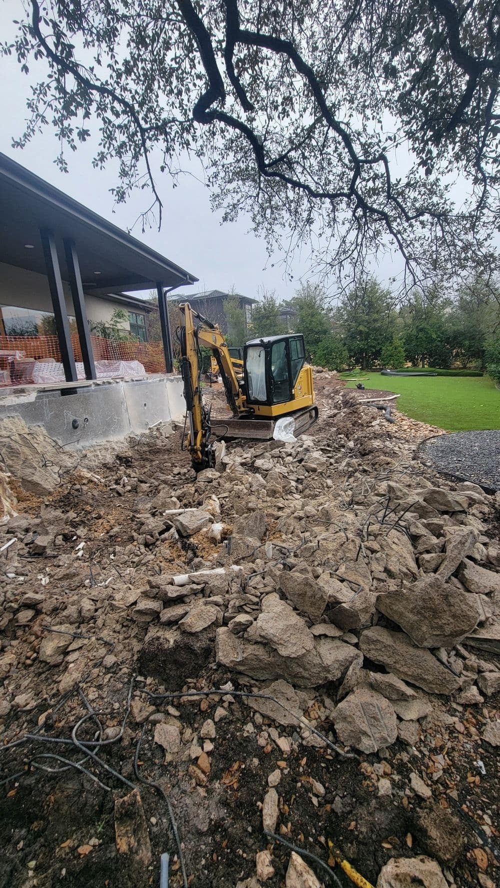 Excavator at a construction site, surrounded by rocks and debris near a building foundation.
